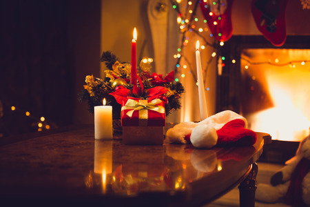 Toned photo of burning candles, fireplace and giftbox at christmas eveの写真素材