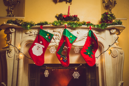 Toned photo of three red Christmas socks hanging on fireplace at houseの写真素材