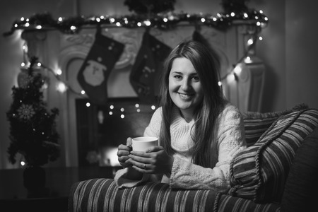 Black and white portrait of smiling woman drinking tea at fireplace at Christmasの写真素材