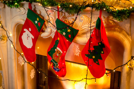Closeup photo of three red christmas socks hanging on burning fireplace
