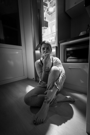 Black and white photo of woman sitting next to fridge at nightの写真素材