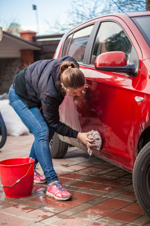 Young slim woman washing red car door with rugの写真素材