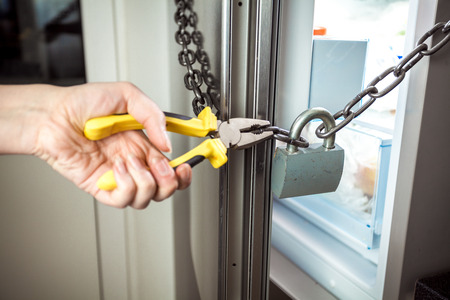 Closeup photo of woman cutting chain on fridge with pliersの写真素材