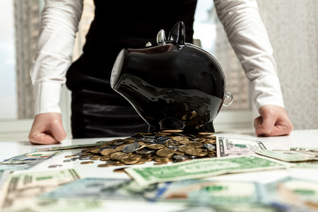 Photo of businesswoman standing behind piggy bank on pile of moneyの写真素材