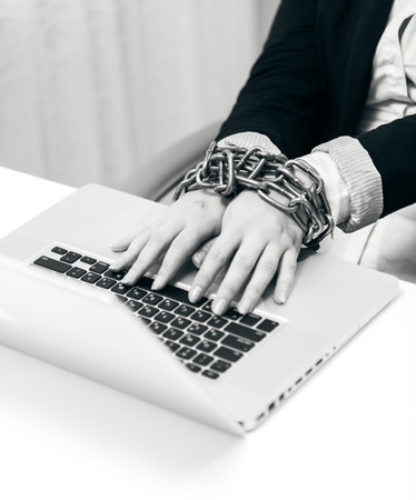 Black and white closeup photo of woman locked to laptop by chainの写真素材