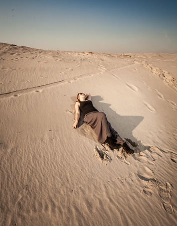 Beautiful woman in dress lying on sand dune at desertの写真素材