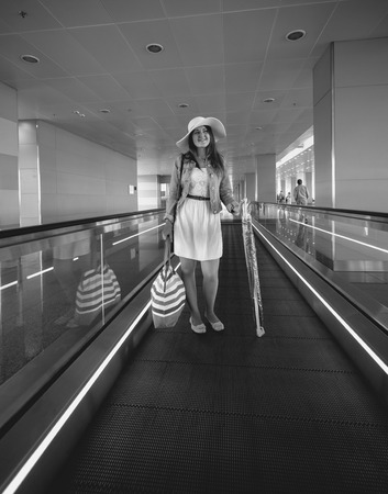 Black and white photo of young beautiful woman standing on escalator at airportの写真素材