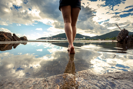 Rear view photo of beautiful slim female legs walking on water surface with reflecting skyの写真素材