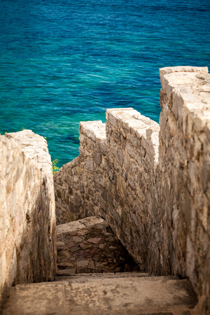 Beautiful ancient stone wall with stairs leading to blue seaの写真素材