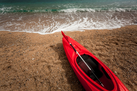 Closeup photo of red kayak on beautiful sandy beach at blue wavy seaの写真素材