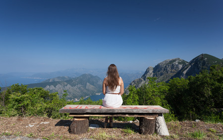Beautiful brunette woman sitting on bench at high mountainの写真素材