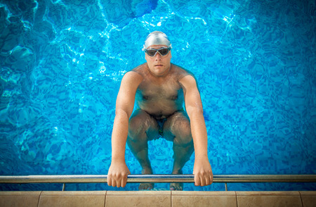 Young male athlete holding on edge of swimming pool and preparing to swimの写真素材