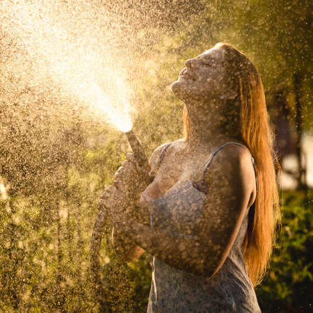 Closeup beautiful portrait of woman with long hair watering garden at sunny dayの写真素材
