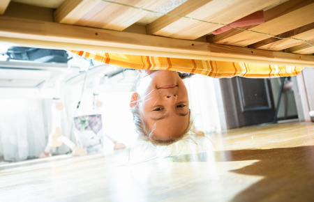 Portrait of brunette smiling girl looking under bed at morningの写真素材
