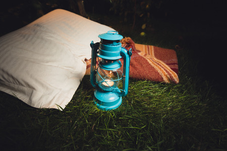 Closeup photo of old lantern, pillow and blanket lying on grass at nightの写真素材