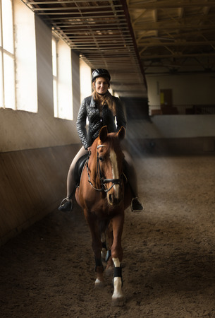 Indoor photo of young woman jockey riding horse on manegeの写真素材