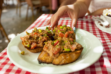 Closeup photo of woman taking bruschetta with tuna from plate at restaurantの写真素材