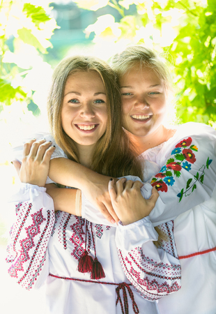 Closeup portrait of two smiling girls in national ukrainian clothes at parkの写真素材