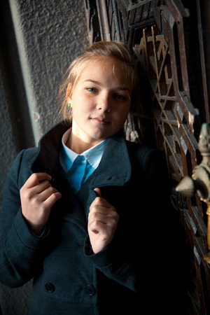 Closeup portrait of sad woman holding collar of black raincoat and leaning against wallの写真素材