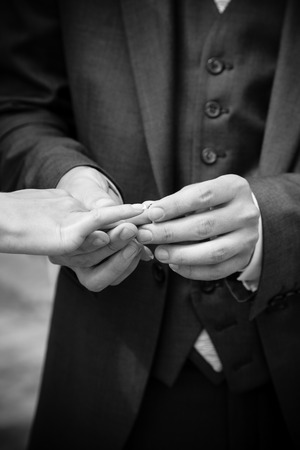 Black and white closeup photo of groom putting ring on brides handの写真素材