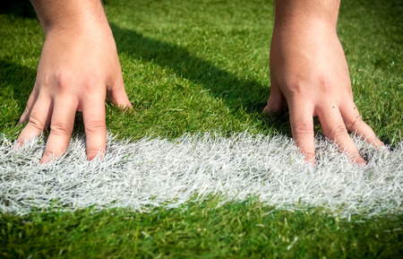 Closeup shot of hands on white start line drawn on grass