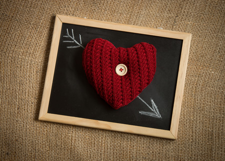 Conceptual shot of knitted heart lying on arrow drawn by chalkの写真素材