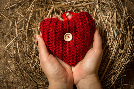 Closeup conceptual photo of woman protecting red knitted heartの写真素材