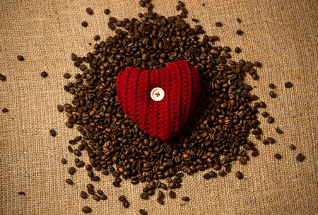 Closeup conceptual photo of red heart lying on pile of coffee beansの写真素材