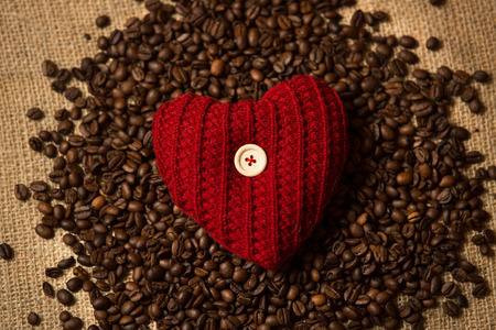 Closeup photo of knitted red heart lying on pile of coffee beansの写真素材