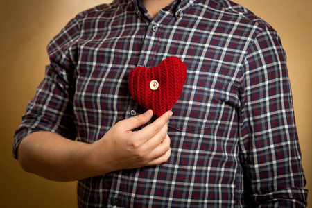 Young man in shirt posing with red knitted heart