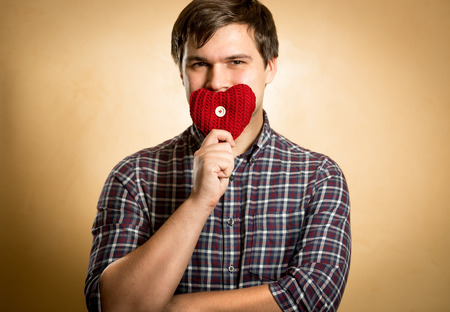 Handsome smiling man holding red heart at mouth