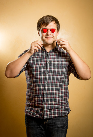Portrait of funny man holding red hearts in front of eyesの写真素材