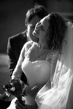 Black and white romantic portrait of groom kissing smiling bride in cheekの写真素材