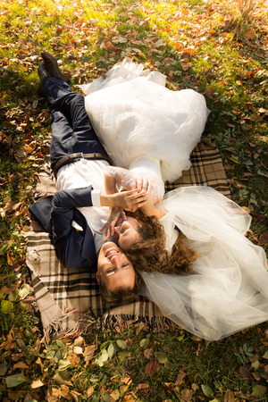 Beautiful just married couple lying on yellow leaves at parkの写真素材