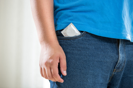 Closeup photo of young man in jeans with condom in pocketの写真素材