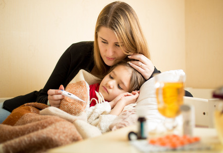 Young mother checking temperature of sick daughter lying in bed Young mother checking temperature of sick daughter lying in bed