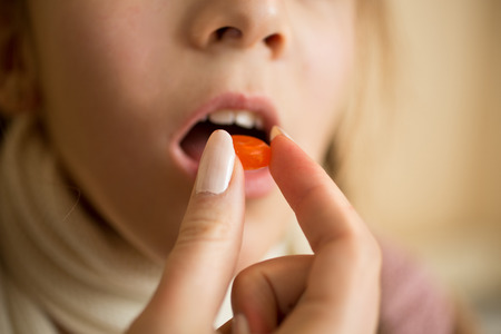Closeup photo of little girl taking medicine in pillの写真素材