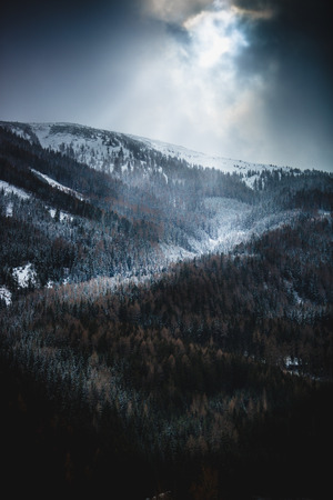 Beautiful view of sun shining through clouds over high snowy mountainsの写真素材