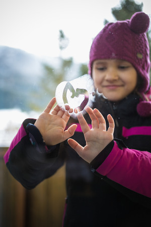Closeup photo of smiling cute girl drawing heart on windowの写真素材