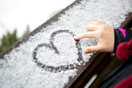 Closeup photo of little girl drawing heart on snowの写真素材