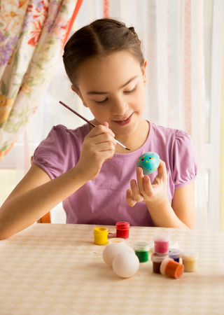 Closeup portrait of cute girl with brush painting Easter eggsの写真素材