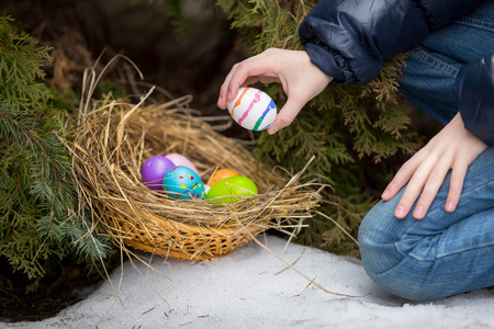 Closeup photo of little girl putting easter egg in nest at cold snowy day