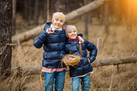 Two smiling girls posing with basket full of Easter eggs at forestの写真素材