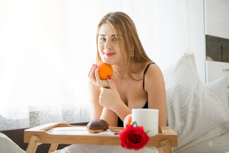 Portrait of beautiful young woman lying in bed and holding orangeの写真素材