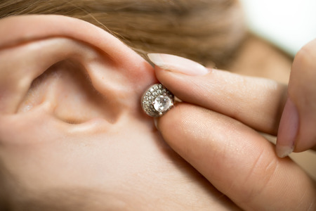 Closeup photo of woman putting earring with diamondsの写真素材