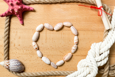 Heart made of seashells with border of ropes and knots on wooden backgroundの写真素材