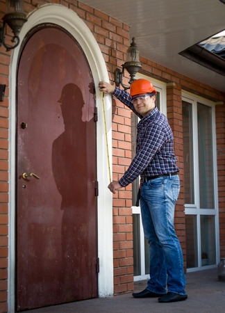 Young professional worker measuring metal door with tapeのeditorial素材