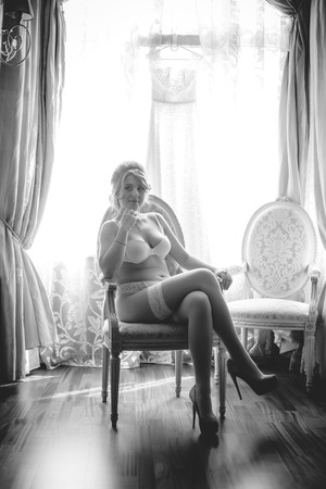 Black and white shot of sexy bride in lingerie sitting in chair against windowの写真素材