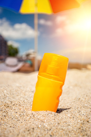 Closeup shot of yellow suntan lotion bottle lying on sand at beachの写真素材