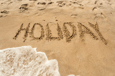 Word "Holiday" written on wet sand on the seashoreの写真素材